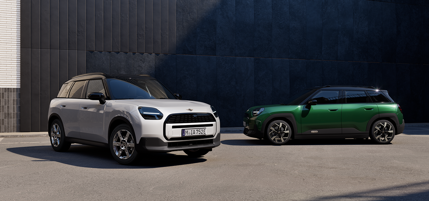 Vue avant et latérale de la MINI Aceman Electric Nanuq White et British Racing Green avec toit noir en ville.