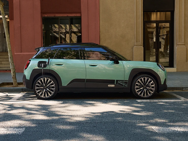 Vue latérale de la MINI Aceman Electric Ocean Wave Green avec toit noir en charge en ville.