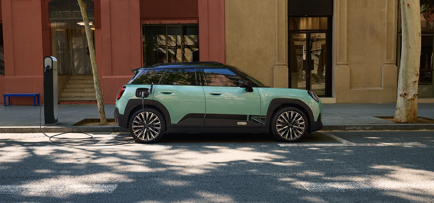 Vue latérale de la MINI Aceman Electric Ocean Wave Green avec toit noir en charge en ville.