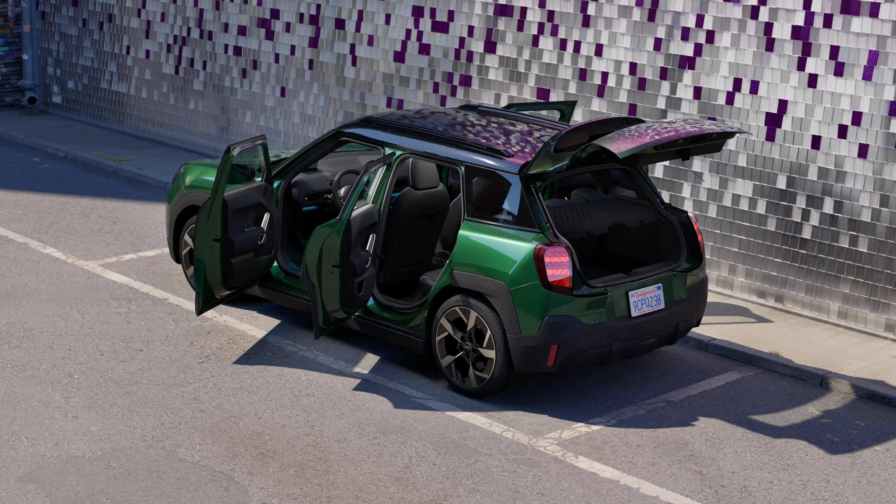Vue latérale arrière de la MINI Aceman 100 % électrique en British Racing Green garée avec toutes les portes ouvertes et un mur coloré en l'arrière-plan