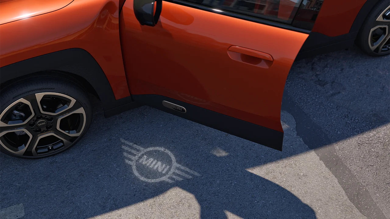 Vue extérieure de la MINI Aceman 100 % électrique avec la porte ouverte et la lumière d'accueil du logo MINI projetée au sol