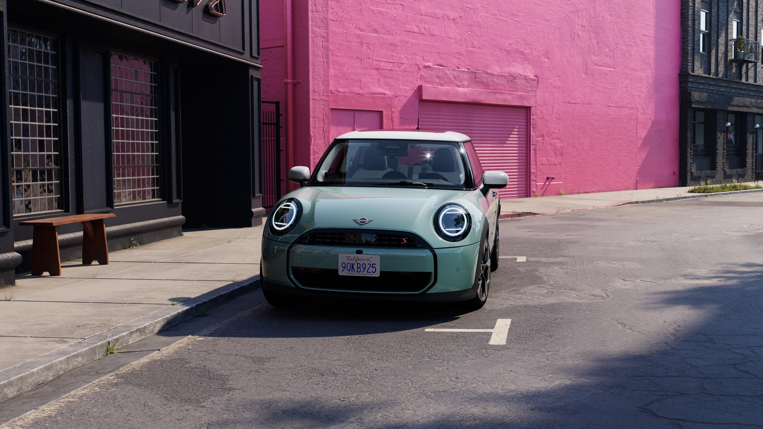 Vue frontale d’une MINI Cooper en Ocean Wave Green et toit blanc en cours de stationnement dans la rue, avec un mur rose en arrière-plan