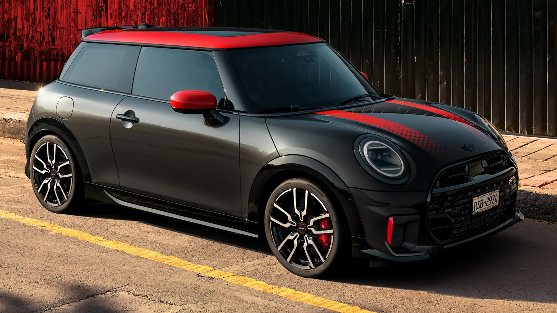 MINI John Cooper Works 3 portes Midnight Black avec toit et coques de rétroviseurs en Chili Red et bandes sportives rouges, vue latérale, garée dans la rue.