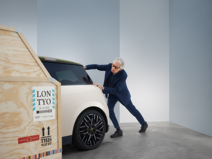 Heckansicht des vollelektrischen MINI Cooper Paul Smith Edition in Inspired White mit Paul Smith hinter dem Auto